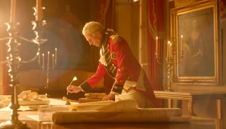 George III bends over a huge table covered in papers, writing with a quill