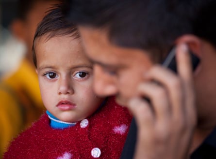 A man holding a small child while talking on a mobile phone in Delhi.