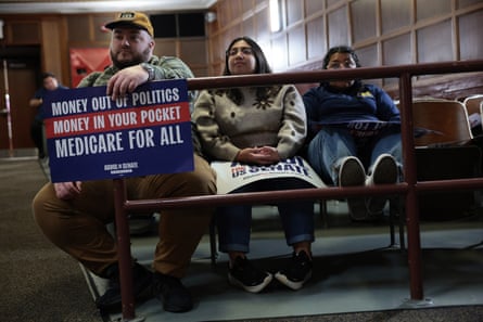 A man, woman and teenager sit in an auditorium holding a political sign.