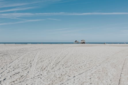 A vast empty white sand beach with a strip of blue sea on the horizon against blue sky