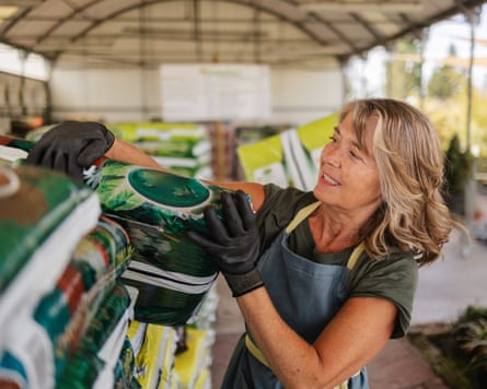 A woman pulling a large bag of soil from a pile in a plant nursery