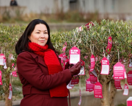 โมนิกา เลนนอน เข้าร่วมการรณรงค์ที่เปิดตัวโดยองค์กร Dignity in Dying Scotland และยืนอยู่หน้าต้นไม้ที่มีป้ายสีแดง เธออายุประมาณ 40 ต้นๆ มีผมดำยาวตรง เธอสวมเสื้อโค้ทสีแดงและผ้าพันคอนิตติ้ง