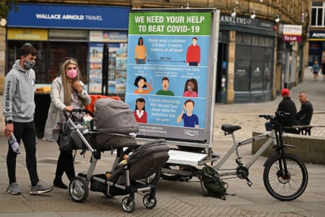 A couple wearing a protective face masks pass a promotion funded by Calderdale Council, an ad bike display advising people on how to slow the spread of the coronavirus, in Halifax in northern England on 9 August, 2020, as local lockdown restrictions are reimposed due to a spike in cases of the novel coronavirus in the town.