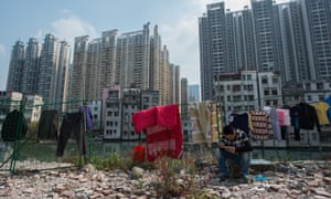 a man sits on a rock as washing hangs on barbed wire nearby with demolished and derelict old housing blocks in the background