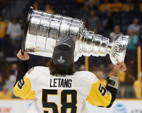 Standing on the ice, he holds the giant trophy on its side