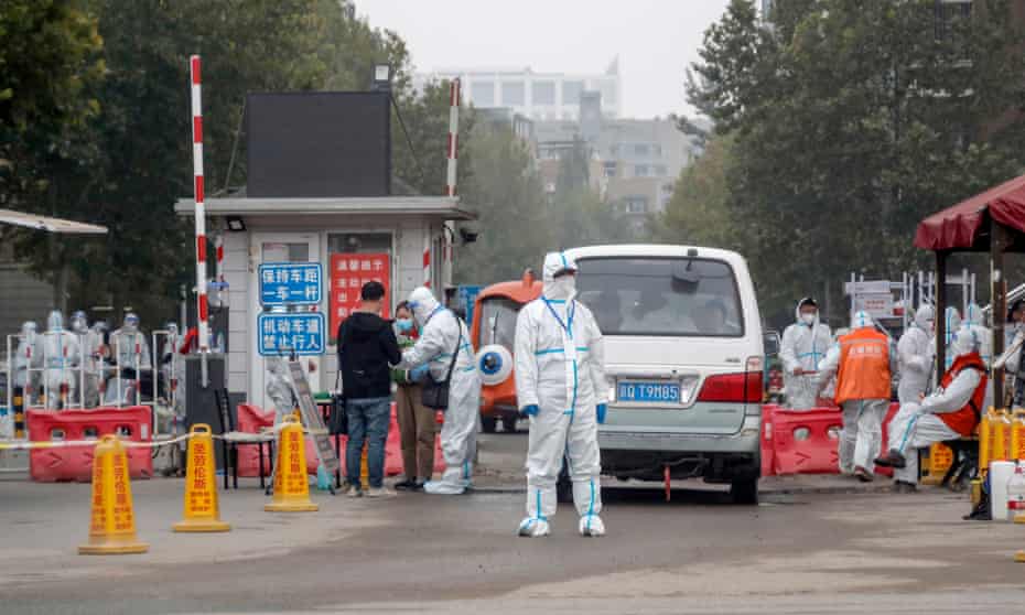 Workers wearing protective suits stand guard at an entrance to a residential neighbourhood in Beijing which is under lockdown due to new Covid cases.