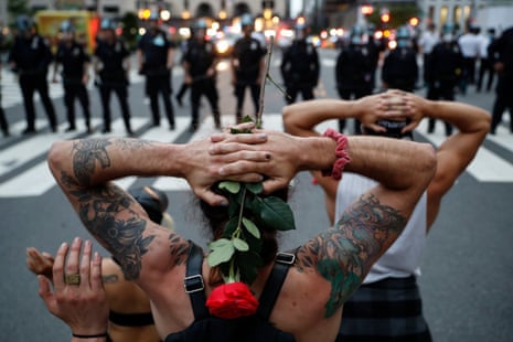 One demonstrator holding rose kneels while hand and another protester are shown in front of police line