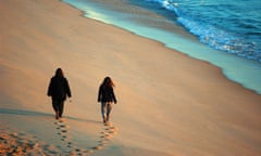 Two people walking along a beach in Merimbula, NSW