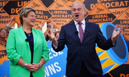 Sarah Dyke clasps her hands and grins at Ed Davey who, in a jacket, shirt and tie, is speaking and gesturing with his hands