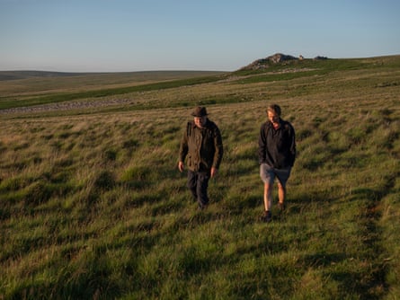 Two men walk across a grassy landscape.