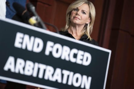 A woman behind a sign the reads ‘End Forced Arbitration’