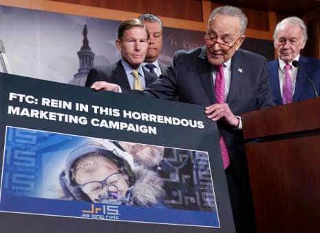Chuck Schumer holds a placard with an ad on it showing a child aiming a gun.
