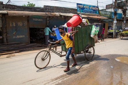 A masked man pushes a waste-laden rickshaw long a street