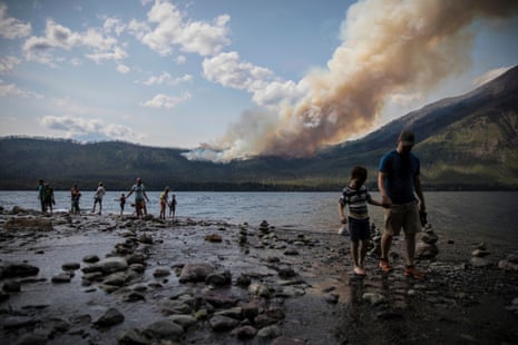 people walking along a shore as fire burns in the distance