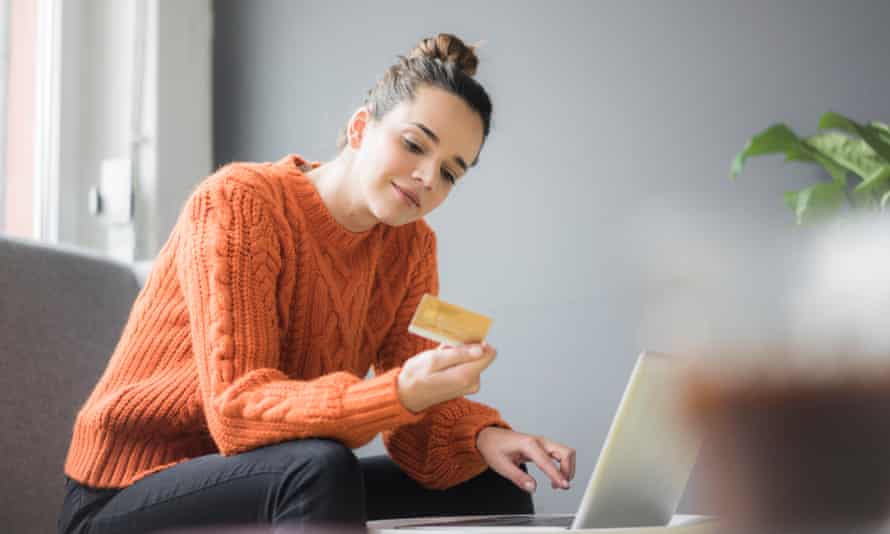 Portrait of content woman sitting on couch using laptop and credit card