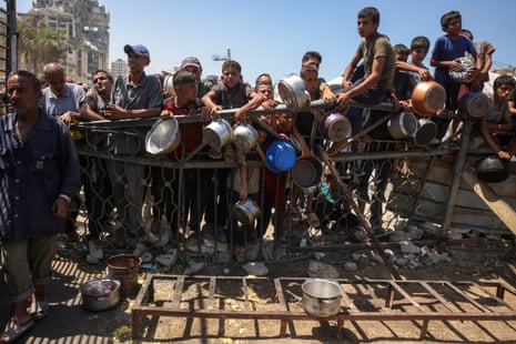 People wait with pots as they try to get rice from a charity kitchen providing food for free in the west of Gaza City.