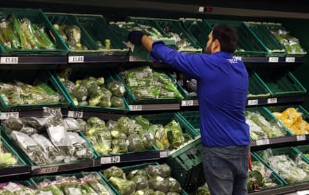A worker stocks vegetables at a supermarket in London.