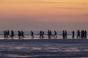 People run in silhouette across a beach at dawn