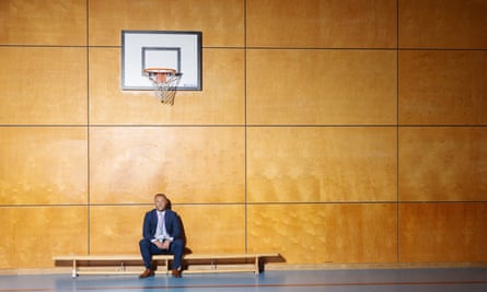 Michael Robson, senior executive at the Northern Education Trust and a former headteacher, standing on a school PE bench with a basketball net above his head