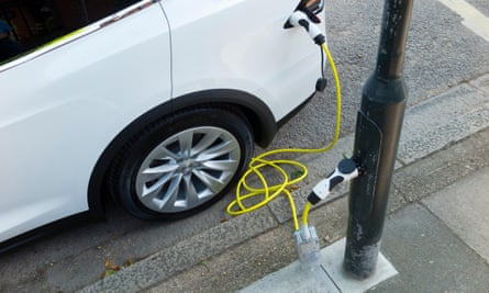 An electric car charges on the street using a yellow-coloured cable plugged into an adapted lamppost