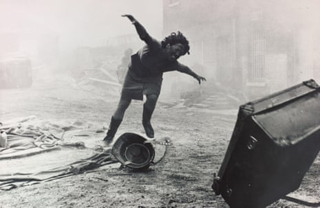 a black and white shot of a child covered in dirt, or soot, arm outstretched, falling to the ground behind a suitcase flying through the air, in a street scene of devastation