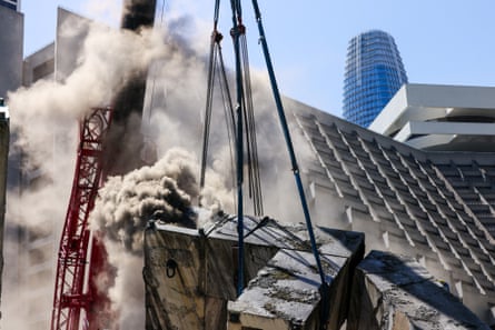 Gray smoke billowing amid a crane, with high rises beyond.