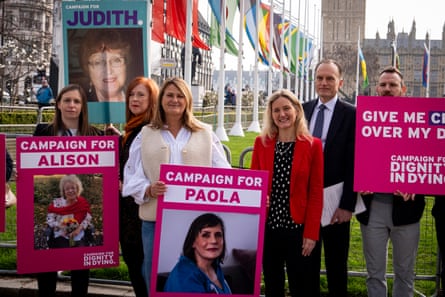 People hold placards and signs supporting assisted dying with the Houses of Parliament in the background