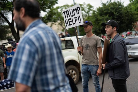 a group of men stand at demonstration, one holding a sign saying 'trump help!!'