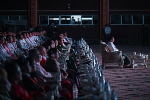 A man sits in a chair, with rows of people on seats behind