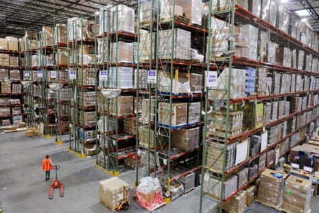 a worker walks alongside rows of packages piled to the ceiling of a giant warehouse