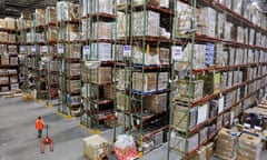 a worker walks alongside rows of packages piled to the ceiling of a giant warehouse