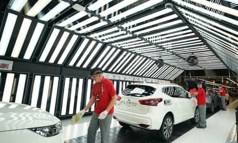 a worker in red top and grey trousers attends to a white car on the production line