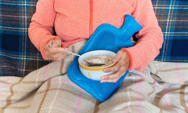 Woman under a blanket with hot-water bottle eating porridge