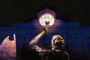 A projection of a statue holding a torch is projected on to a building