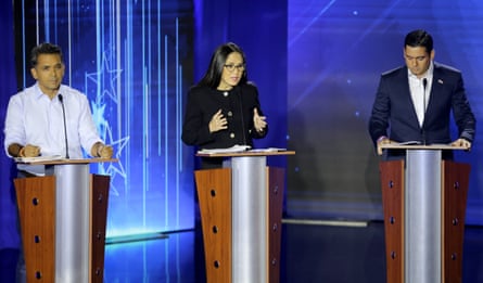 Two men and a woman stand at lecterns during a televised debate 