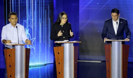 Two men and a woman stand at lecterns during a televised debate
