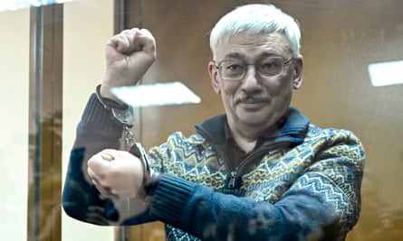 Oleg Orlov stands in handcuffs behind a glass screen in a Russian courtroom.