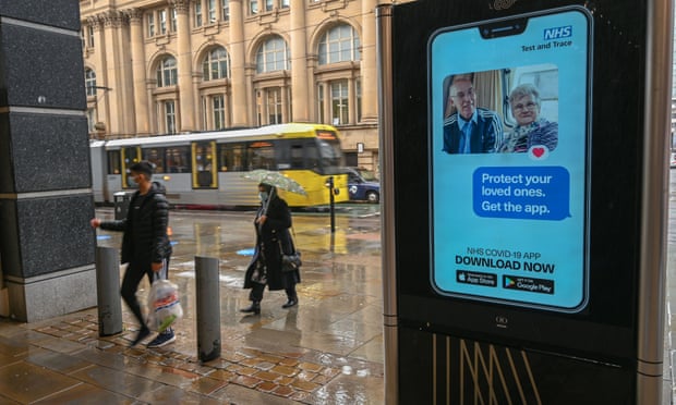People in Manchester walk past an electronic sign asking them to download the NHS test and trace app
