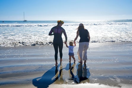 two sisters walk with a young child on a beach