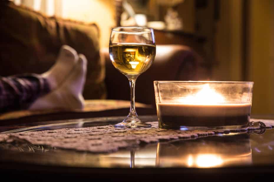 Wine glass and candle in a relaxing scene with person's feet on a sofa in the background