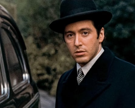 Closeup of Pacino who wears a black hat and coat