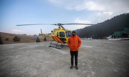 Aşağı ceketli ciddi görünümlü bir adam sarı bir helikopterin önünde duruyor