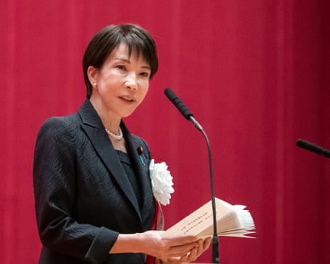 Japanese PM Sanae Takaichi speaking against a red backdrop