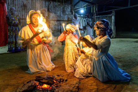 A nun and girls carrying candles praying around the fire with their faces painted white during a Bwiti initiation ceremony.