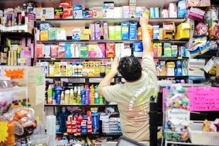 A clerk grabs a yellowish supplement container from a wall of medicine supplements and toiletries