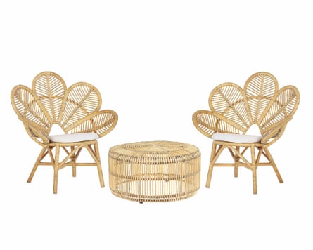 Two rattan woven chairs. The chair backs comprise 5 petal to form a shell shape. Each chair has a white cushion. In between the chairs is a circular low table which is made of rattan.