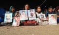 Children sit on the ground holding posters of their loved ones.