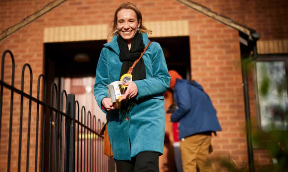 Smiling woman with a Lib Dem badge walks past a redbrick building