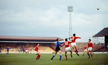 Players in red and blue jump to contest a high ball in an old photograph of a football match 