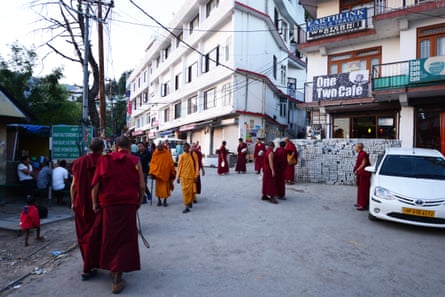 A road with a single white car and small groups of monks on foot wearing burgundy or saffron robes.